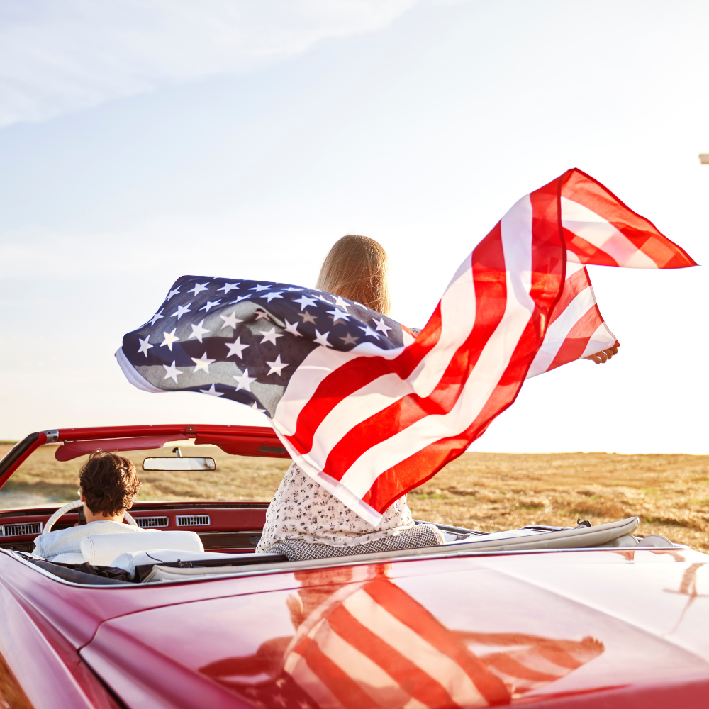 A couple in a convertible on route 66 with a US flag waving
