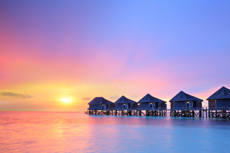A hotel in The Maldives on a beach and the sea with the sun setting