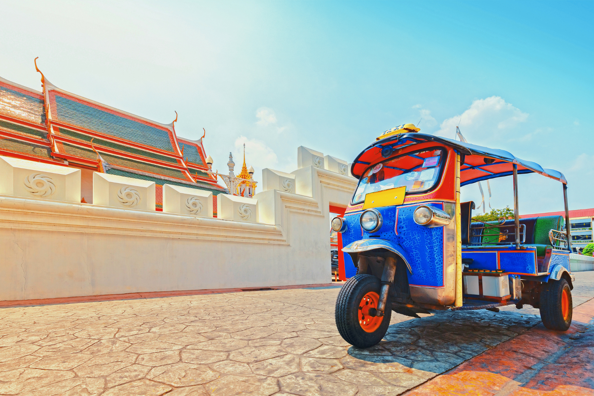 A blue and red tuk tuk in Bangkok next to the palace walls